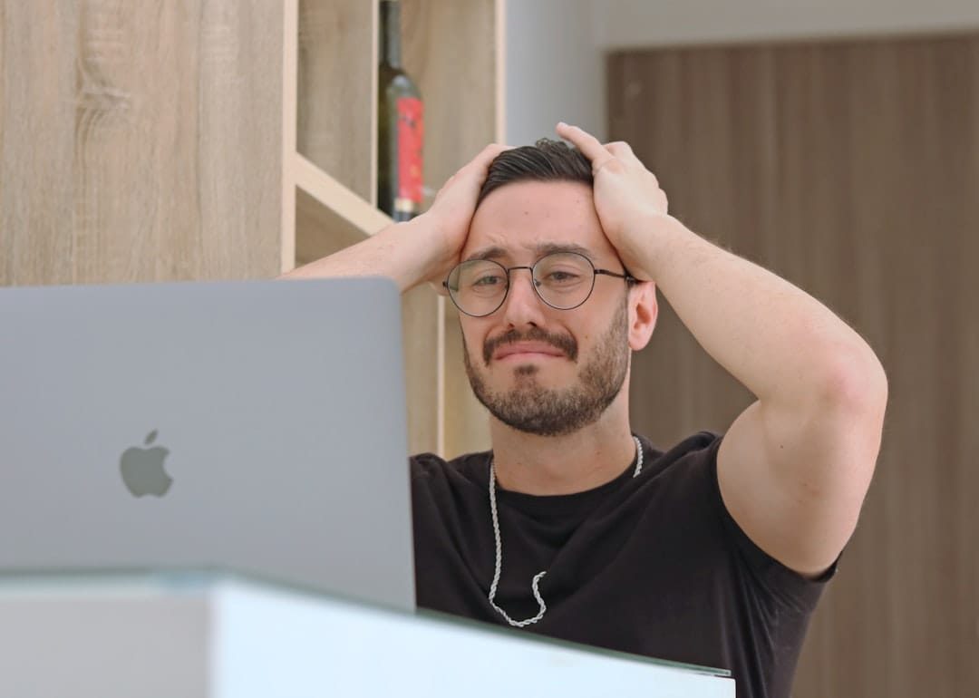 Frustrated man with hands on head staring at MacBook screen after hitting Google Drive download quota error. Photo by Unsplash.